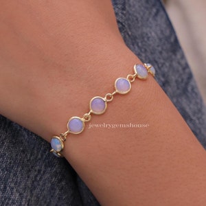 Può includere: Un braccialetto d'oro con una catena di piccole pietre rotonde di opale blu chiaro. Il braccialetto è al polso.