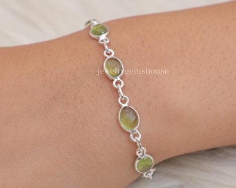 May include: A silver chain bracelet featuring four oval-shaped, light green translucent gemstones set in polished metal bezels. The links are connected by small circular silver rings, creating a delicate and uniform design that wraps around the wrist.