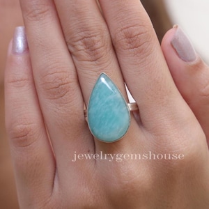 Może przedstawiać: Pierścionek w kształcie łzy z jasnoniebieskim kamieniem szlachetnym osadzonym w srebrze próby 925. Pierścionek jest na palcu.