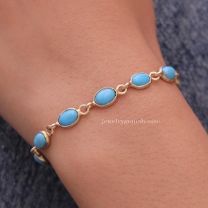 Könnte beinhalten: Ein goldenes Kettenarmband mit ovalen türkisfarbenen Steinen. Das Armband befindet sich an einem Handgelenk.