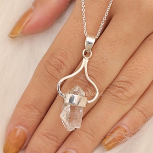 May include: A silver necklace with a clear quartz crystal pendant. The pendant is set in a silver heart-shaped frame.