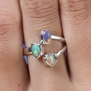Könnte beinhalten: Ein silberner Ring mit drei Opal-Steinen. Die Steine sind in verschiedenen Formen und Größen und in einem zarten, offenen Design gefasst.