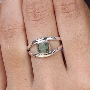 May include: A silver ring with a green gemstone set in a square shape. The ring has a double band design.