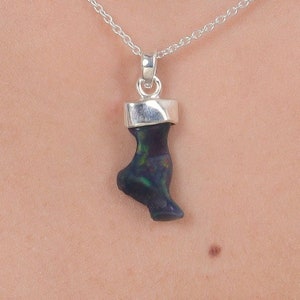 May include: A pendant necklace featuring a dark, iridescent opal stone carved into the shape of a foot, suspended from a polished silver bail and a delicate silver chain. The opal displays flashes of green and red color against a dark base.