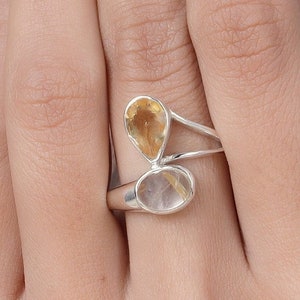 Peut inclure: Une bague en argent avec deux pierres précieuses en forme de goutte. La plus grande pierre est claire avec des reflets dorés, et la plus petite pierre est de couleur ambre clair.