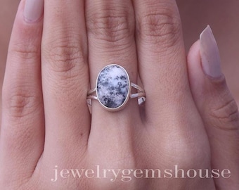 Puede incluir: Un anillo de plata con una piedra ovalada de patrón moteado en blanco y gris oscuro. La banda tiene un diseño dividido donde se une al engaste de la piedra. El texto "jewelrygemshouse" está impreso en blanco en la parte inferior de la imagen.
