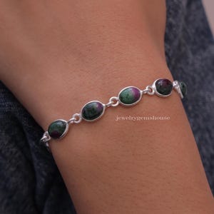 May include: A silver bracelet featuring oval-shaped green and pink gemstones. The bracelet has a delicate chain and is accented with small silver beads.