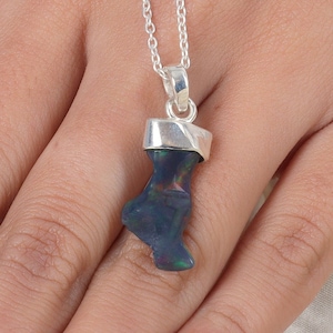 May include: A pendant featuring a dark, iridescent raw opal stone with flashes of green and red, set in a polished silver cap and suspended from a delicate silver chain. The stone has an irregular, organic shape and a smooth, reflective surface.