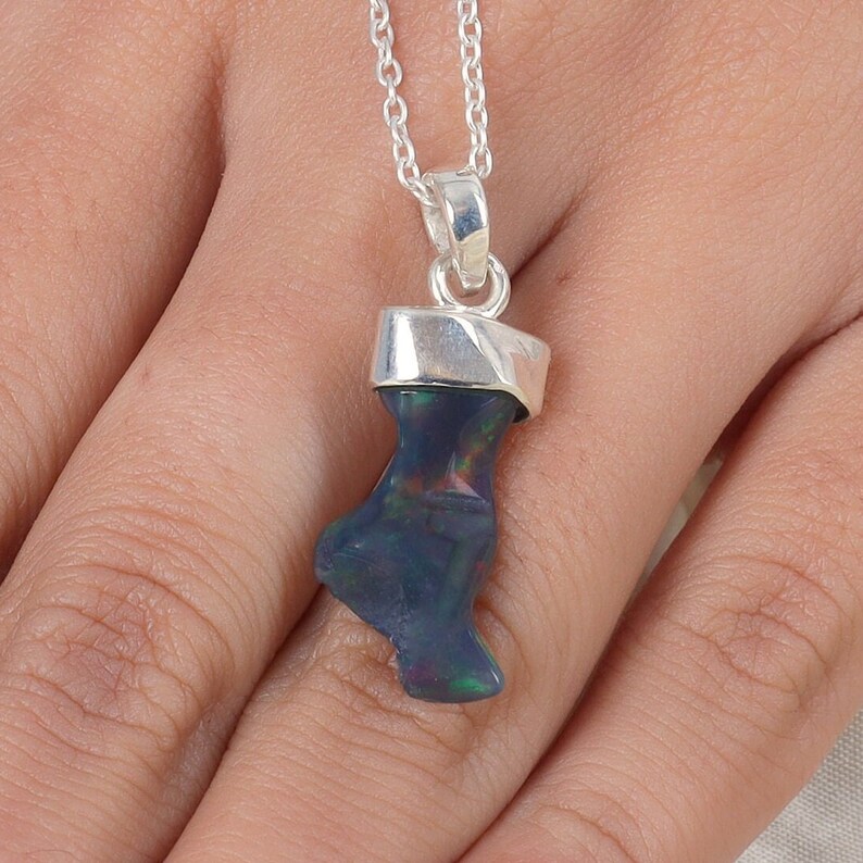 May include: A pendant featuring a dark, iridescent raw opal stone with flashes of green and red, set in a polished silver cap and suspended from a delicate silver chain. The stone has an irregular, organic shape and a smooth, reflective surface.