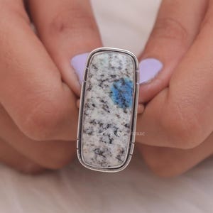 May include: A silver ring with a rectangular blue and white stone. The stone has a speckled pattern.