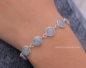 May include: A silver bracelet featuring round, pale blue gemstones. The bracelet is composed of linked silver settings, each holding a single stone. The jewelry is displayed on a person's wrist.