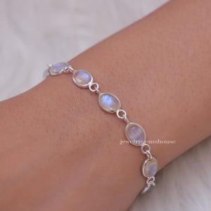 May include: A silver bracelet with oval-shaped moonstone beads. The bracelet is on a person's wrist.