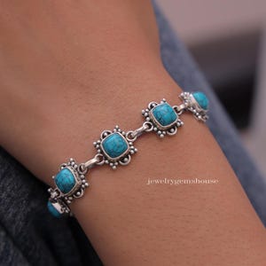 Peut inclure: Bracelet en argent orné de pierres turquoises carrées. Chaque pierre est sertie dans un cadre décoratif et orné. Le bracelet est présenté sur un poignet, mettant en valeur le design et la couleur du bijou.