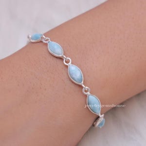 Puede incluir: Una pulsera de plata con piedras preciosas ovaladas de color azul claro. Las piedras est&aacute;n unidas por peque&ntilde;os conectores de plata. La pulsera se lleva en la mu&ntilde;eca. El texto "jewelrygemshouse" es visible.
