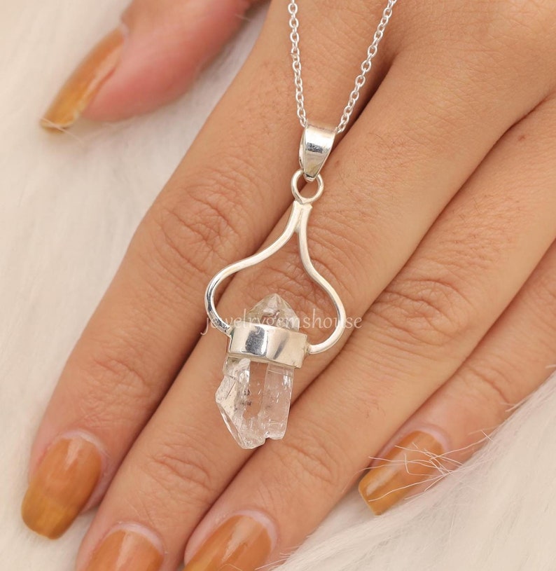 May include: A silver necklace with a clear quartz crystal pendant. The pendant is set in a silver heart-shaped frame.