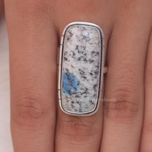 May include: A silver ring with a rectangular blue and white stone. The stone has a speckled pattern.