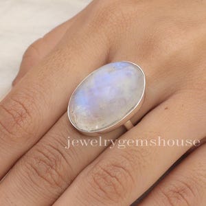May include: A silver ring featuring a large oval moonstone. The stone has a milky white colour with iridescent blue and white flashes.