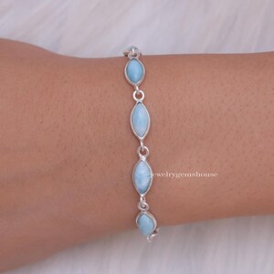 Puede incluir: Una pulsera de plata con piedras preciosas ovaladas de color azul claro. Las piedras est&aacute;n unidas por peque&ntilde;os conectores de plata. La pulsera se muestra en una mu&ntilde;eca.