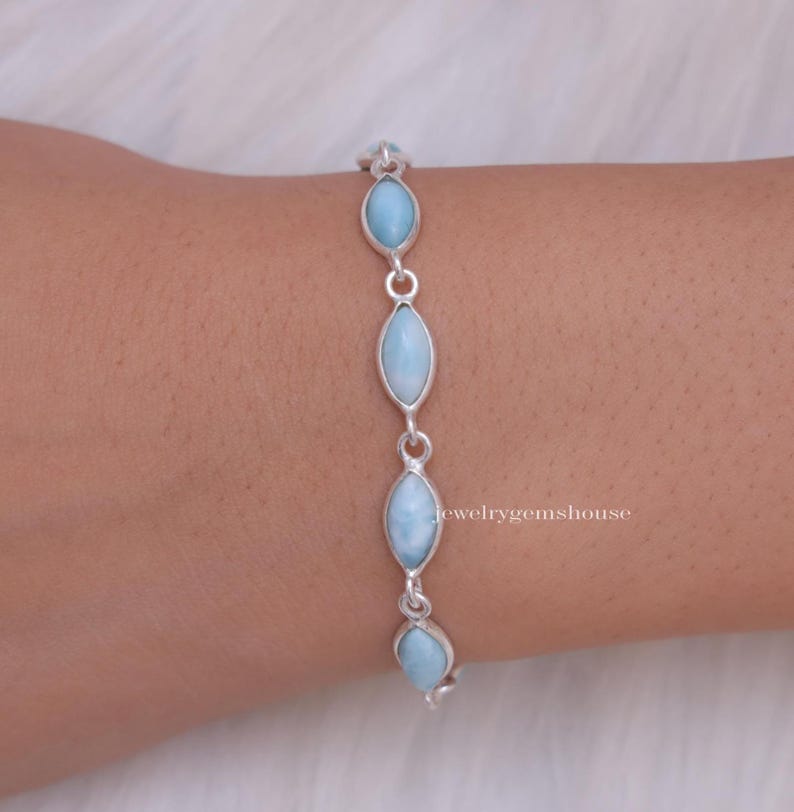 Puede incluir: Una pulsera de plata con piedras preciosas ovaladas de color azul claro. Las piedras est&aacute;n unidas por peque&ntilde;os conectores de plata. La pulsera se muestra en una mu&ntilde;eca.