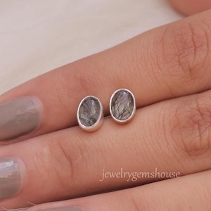 May include: A pair of silver stud earrings with oval-shaped black and clear quartz stones.