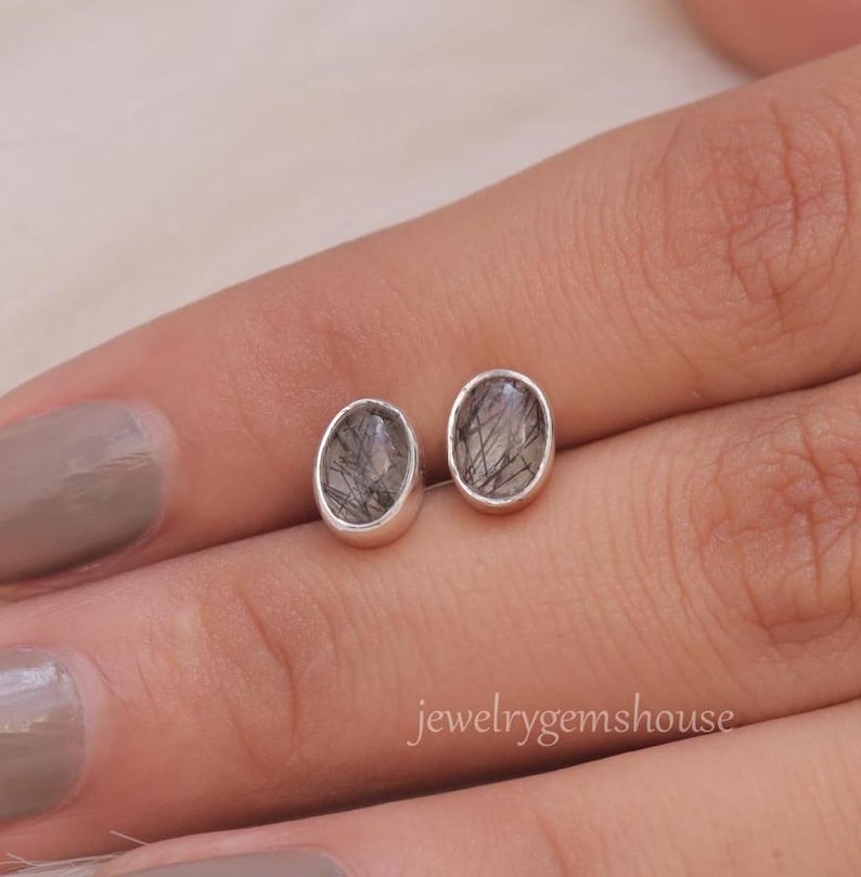 May include: A pair of silver stud earrings with oval-shaped black and clear quartz stones.