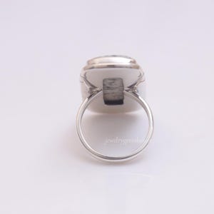 May include: A silver ring with a white oval gemstone. The ring is set in a simple, elegant design.