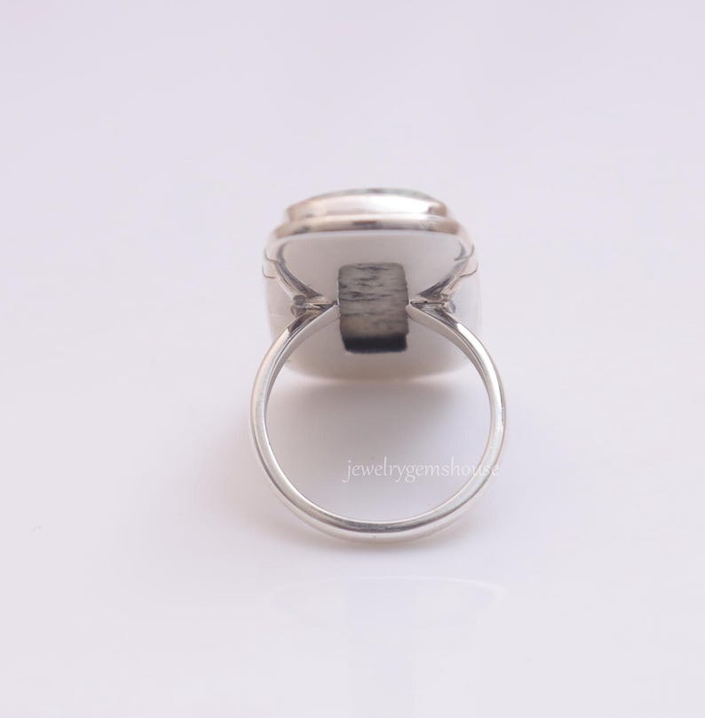May include: A silver ring with a white oval gemstone. The ring is set in a simple, elegant design.