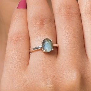 May include: A silver ring with a large oval-shaped labradorite gemstone. The gemstone has a dark blue and green color with iridescent flashes.