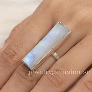 May include: A silver ring with a rectangular moonstone set in a silver band. The ring is on a finger.