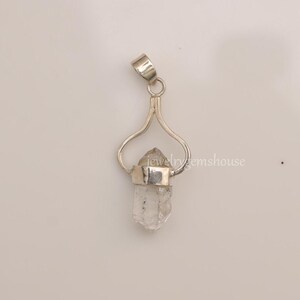 May include: A silver pendant featuring a clear quartz crystal point. The crystal is set in a silver bezel and hangs from a delicate silver bail.