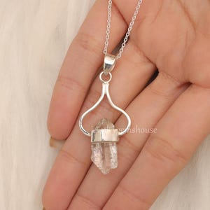 May include: A silver necklace with a clear quartz crystal pendant. The pendant is held in a silver heart-shaped frame.