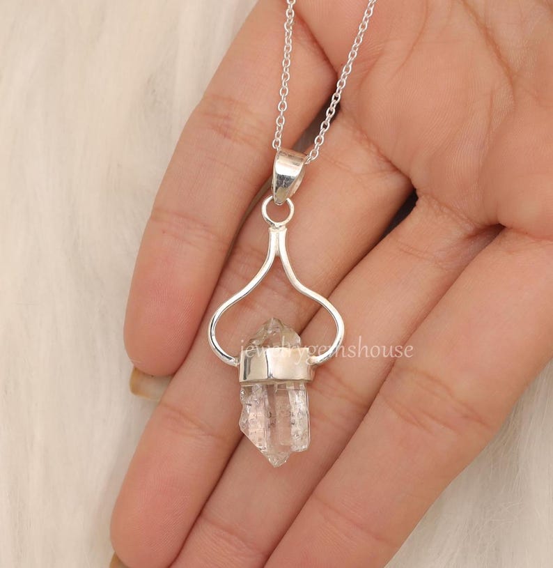 May include: A silver necklace with a clear quartz crystal pendant. The pendant is held in a silver heart-shaped frame.