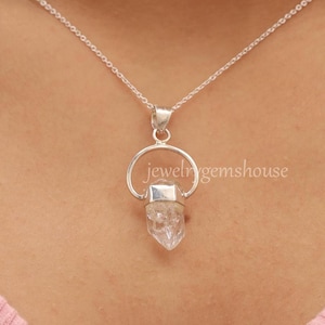 May include: A silver chain necklace with a clear quartz crystal pendant. The pendant is held in a silver ring.