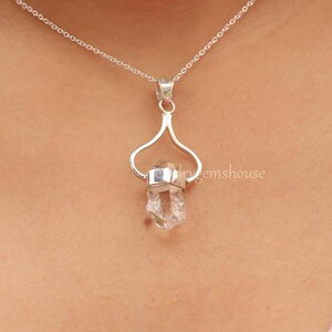 May include: A silver necklace with a clear quartz crystal pendant. The pendant is held in a silver setting that resembles a heart shape.