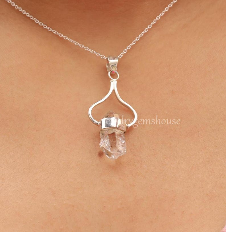May include: A silver necklace with a clear quartz crystal pendant. The pendant is held in a silver setting that resembles a heart shape.