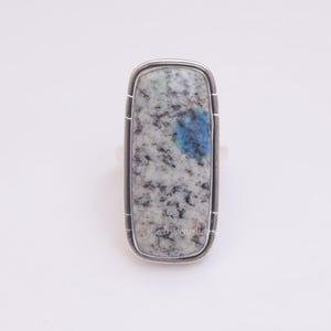May include: A silver ring with a rectangular blue and white stone set in a silver bezel. The stone has a mottled pattern of blue and white.