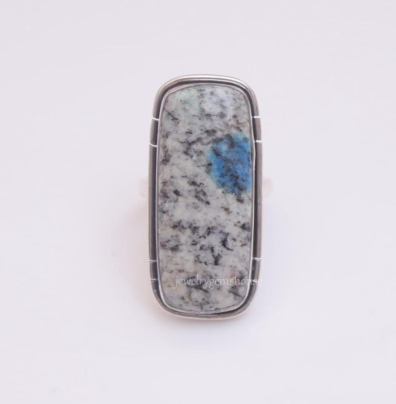 May include: A silver ring with a rectangular blue and white stone set in a silver bezel. The stone has a mottled pattern of blue and white.