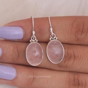 May include: A pair of silver dangle earrings with oval-shaped pink rose quartz stones.