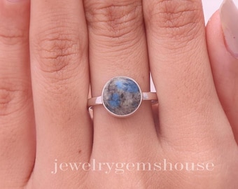 Puede incluir: Un anillo de plata con una piedra redonda azul y gris. El anillo está en un dedo.