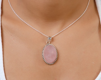 May include: A silver chain necklace with a pink oval pendant. The pendant is set in a silver bezel and has a delicate beaded edge.