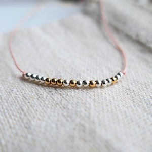 Peut inclure: Un collier délicat avec un cordon rose et des perles argentées et dorées alternées.