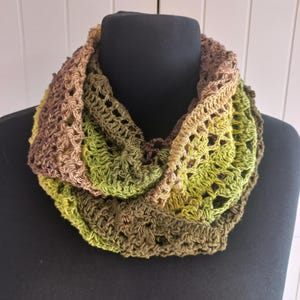 Könnte beinhalten: Ein gehäkelter Infinity-Schal mit einem durchbrochenen Muster und einem Farbverlauf in den Tönen Dunkelbraun, Olivgrün, Limettengrün und Hellbraun. Das kreisförmige Accessoire ist in mehreren Lagen um den Hals drapiert.