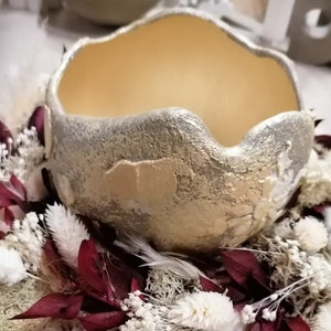 Könnte beinhalten: Eine goldfarbene Keramikschale mit strukturierter Oberfläche, umgeben von weißen und burgunderfarbenen Trockenblumen.