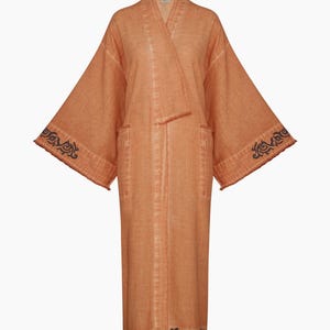 Pode incluir: Uma longa bata de algod&atilde;o laranja com detalhes bordados pretos em torno das mangas e da bainha.