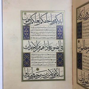 K&ouml;nnte beinhalten: Eine Seite aus einem illuminierten Manuskript mit komplexer arabischer Kalligrafie in schwarzer Tinte. Der Text ist von dekorativen R&auml;ndern mit blauen, goldenen und wei&szlig;en Blumenmustern umrahmt. Die Seite ist cremefarben und vertikal angelegt.