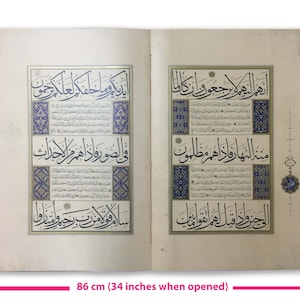 K&ouml;nnte beinhalten: Ein aufgeschlagenes Buch mit komplexer arabischer Kalligrafie auf zwei Seiten, umrahmt von blauen und goldenen Zierr&auml;ndern. Das Buch misst im ge&ouml;ffneten Zustand 62 cm mal 86 cm. Die Seiten enthalten schwarzen Text und detaillierte florale Motive.
