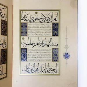 K&ouml;nnte beinhalten: Eine Seite aus einem illuminierten Manuskript mit komplexer arabischer Kalligrafie in schwarzer Tinte. Der Text ist von dekorativen R&auml;ndern in Blau, Gold und Wei&szlig; umrahmt, wobei florale und geometrische Muster die zentrale Schrift umgeben.