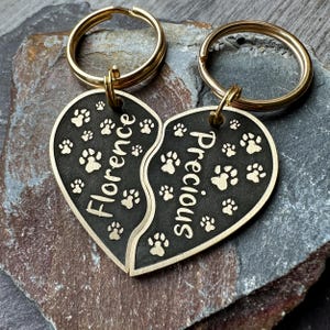 May include: Two gold keyrings with black heart-shaped charms. The charms are split in half and engraved with the names "Florence" and "Precious" and paw prints.