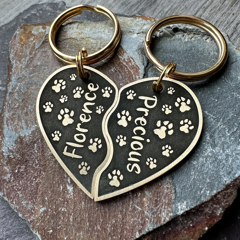 May include: Two gold keyrings with black heart-shaped charms. The charms are split in half and engraved with the names "Florence" and "Precious" and paw prints.