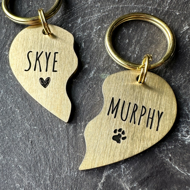Puede incluir: Dos medallas para perros en forma de coraz&oacute;n de oro con anillos partidos. Una medalla dice "SKYE" con un peque&ntilde;o s&iacute;mbolo de coraz&oacute;n. La otra medalla dice "MURPHY" con un s&iacute;mbolo de huella de pata.